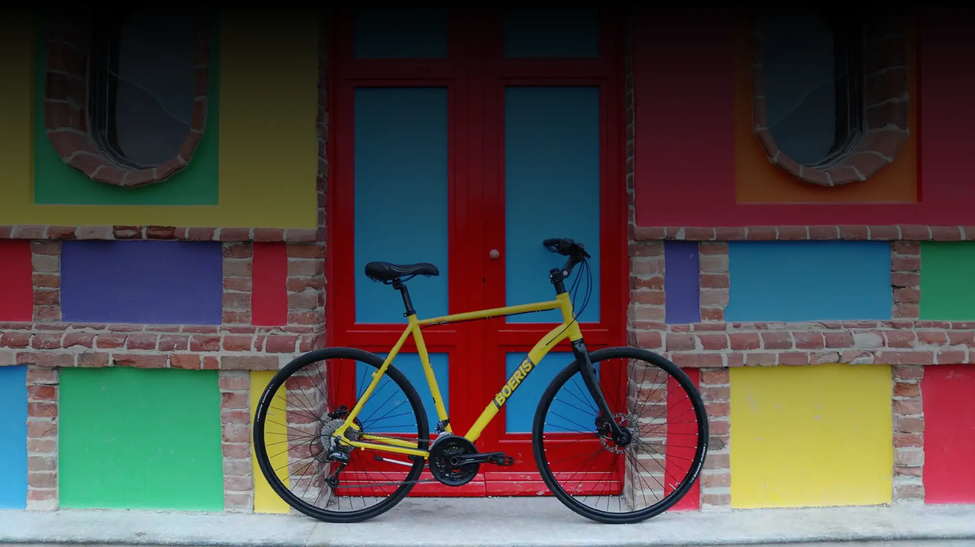 Bicicletta da strada gialla di Boeris Bikes Torino appoggiata ad una porta rossa e azzurra e un muro di mattoni colorato