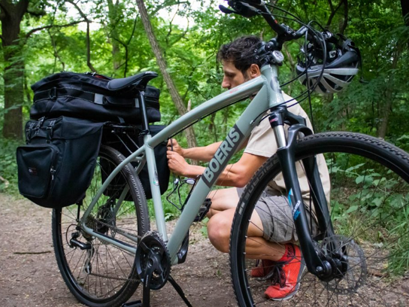 ragazzo con la sua trekking bike Bikepacking bike verde di Boeris Biks Torino su una strada sterrata in un bosco mentre allaccia la la sua borsa bikepacing blu 