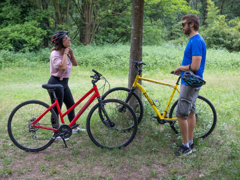 Un ragazzo e una ragazza in mezzo ad un bosco, vicino ad un albero, con le loro trekking bike Lite Weight Tour di Boeris Bikes Torino di colore rosso e giallo