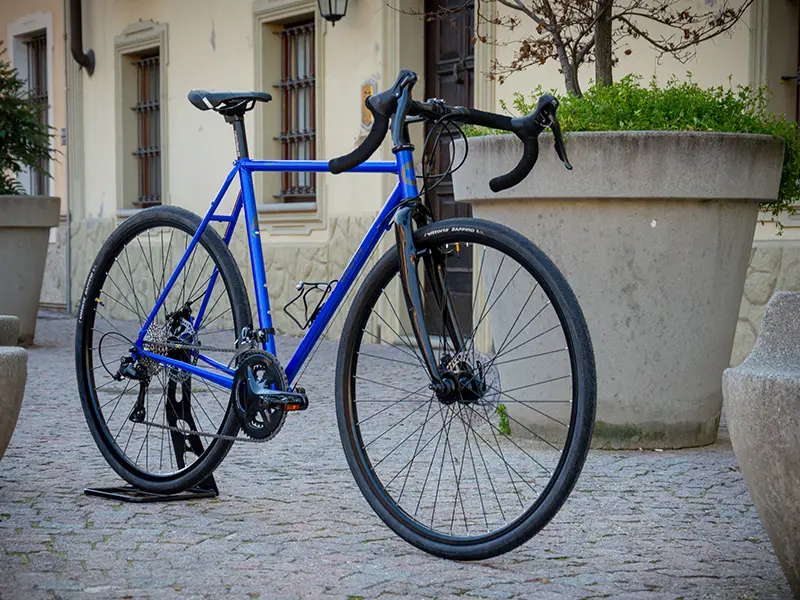 Gravel bike  color blu  con sella e manubrio neri di Boeris Bikes Torino su un cubettato vicino a fioriere