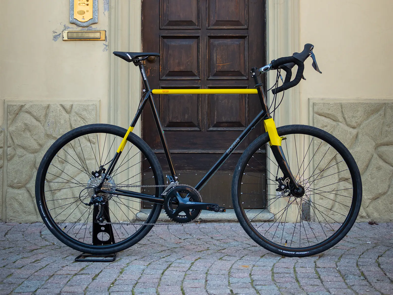 Gravel bike color nera e gialla di Boeris Bikes Torino su un cubettato davanti ad una porta