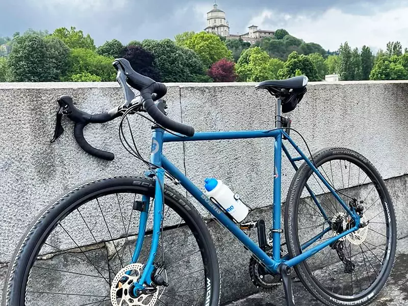 una gravel serie x blu Boeris Bikes Torino appoggiata a un muretto sul lungo Po. Sullo sfondo il Monte dei Cappuccini