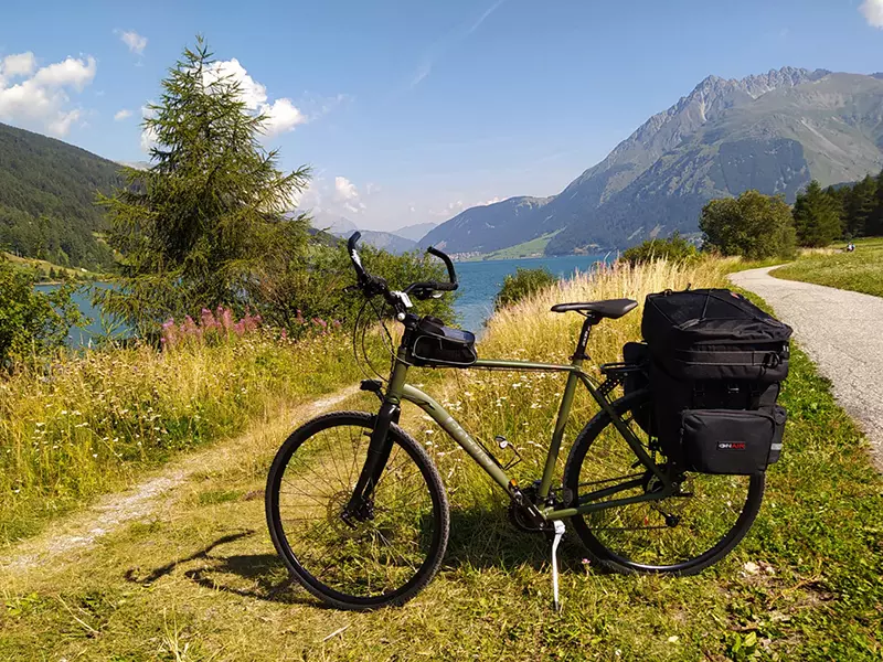 Trekking Bike Boeris Bike Torino verde militare con Bikepacking in un prato di fianco ad una strada. Sullo sfondo un lago e le montagne