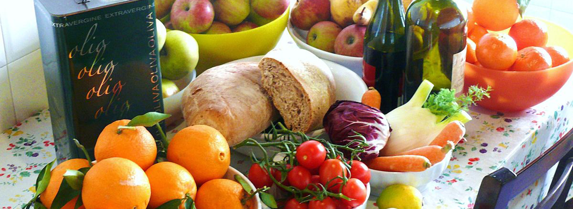Varietà di cibo che fanno parte della dieta mediterranea, come pane olio d'oliva, mele, arance, pomodorini carote per l'articolo Carboidrati: Buoni compagni di Viaggio? alla scoperta dei carboidrati e della dieta Mediterranea