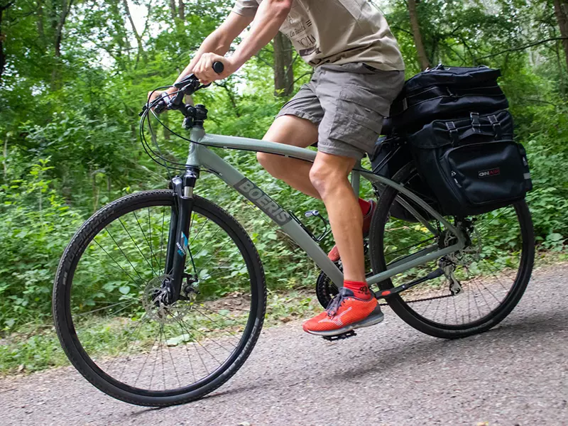 Ragazzo vestito estivo su una Trekking Bike Bikepacking Travel verde con Bikepack fotografata su una strada sterrata in un bosco