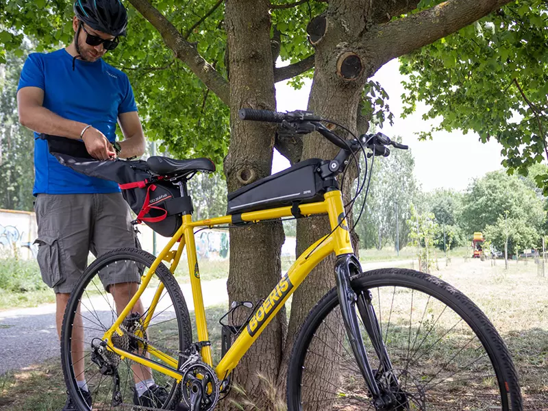 Ragazzo che attrezza i bikepacking della sua trekking bike lite weight tour giallo Boeris Bikes Torino, appoggiata ad un albero in un parco cittadino