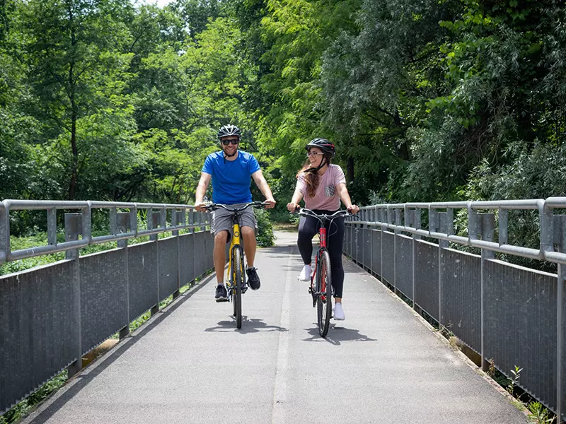 Un ragazzo e una ragazza felici in sella alle loro trekking bike lite weight tour gialla e rossa percorrendo una pista ciclabile