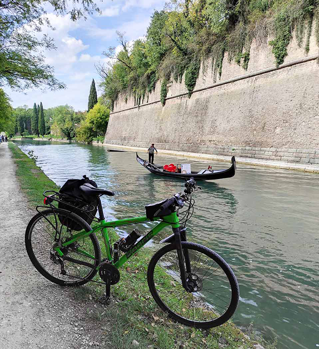 Bici verde Boeris Bikes Torino vicino alle mura della Fortezza veneziana di Peschiera, circondate da acqua e navigate da una gondola