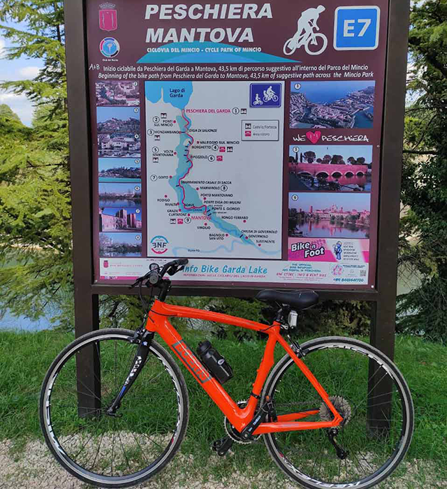 Bici arancione Boeris Bikes Torino appoggiata alla Segnaletica del percorso E7 Peschiera Mantova