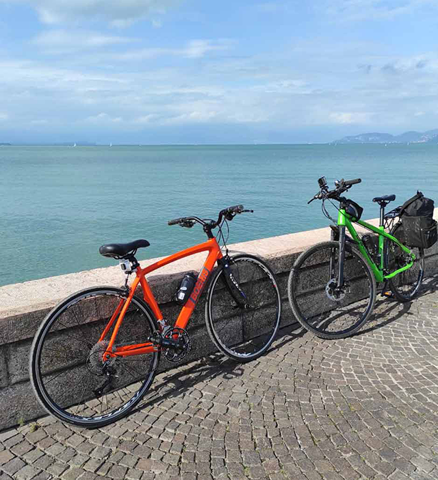 Due biciclette Boeris Bikes Torino una arncione e l'altra verde appoggiati su un muretto sul lungo lago del Lago di Garda