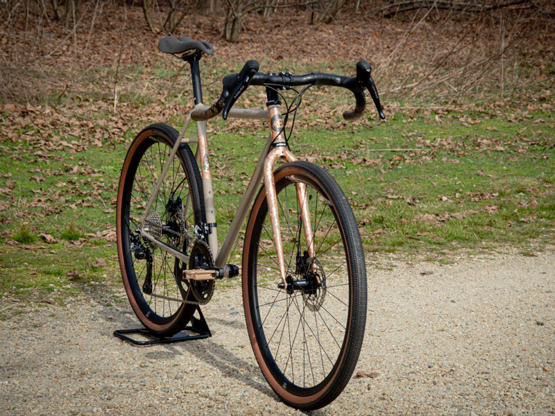 Primo piano frontale della bici Gravel color ruggine in uno sterrato appoggita su un cavalletto