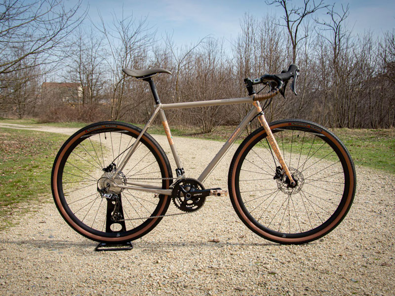 Bici gravel color ruggine in un parco cittadino appoggiata su un cavalletto. 