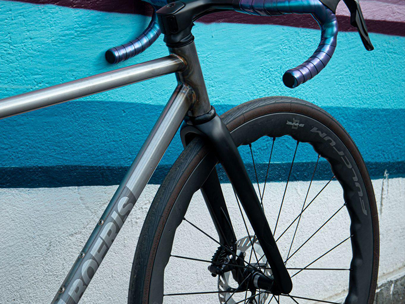 Bici da strada Nordend Boeris Bikes Torino Nera e Blu appoggiata ad un murales azzurro