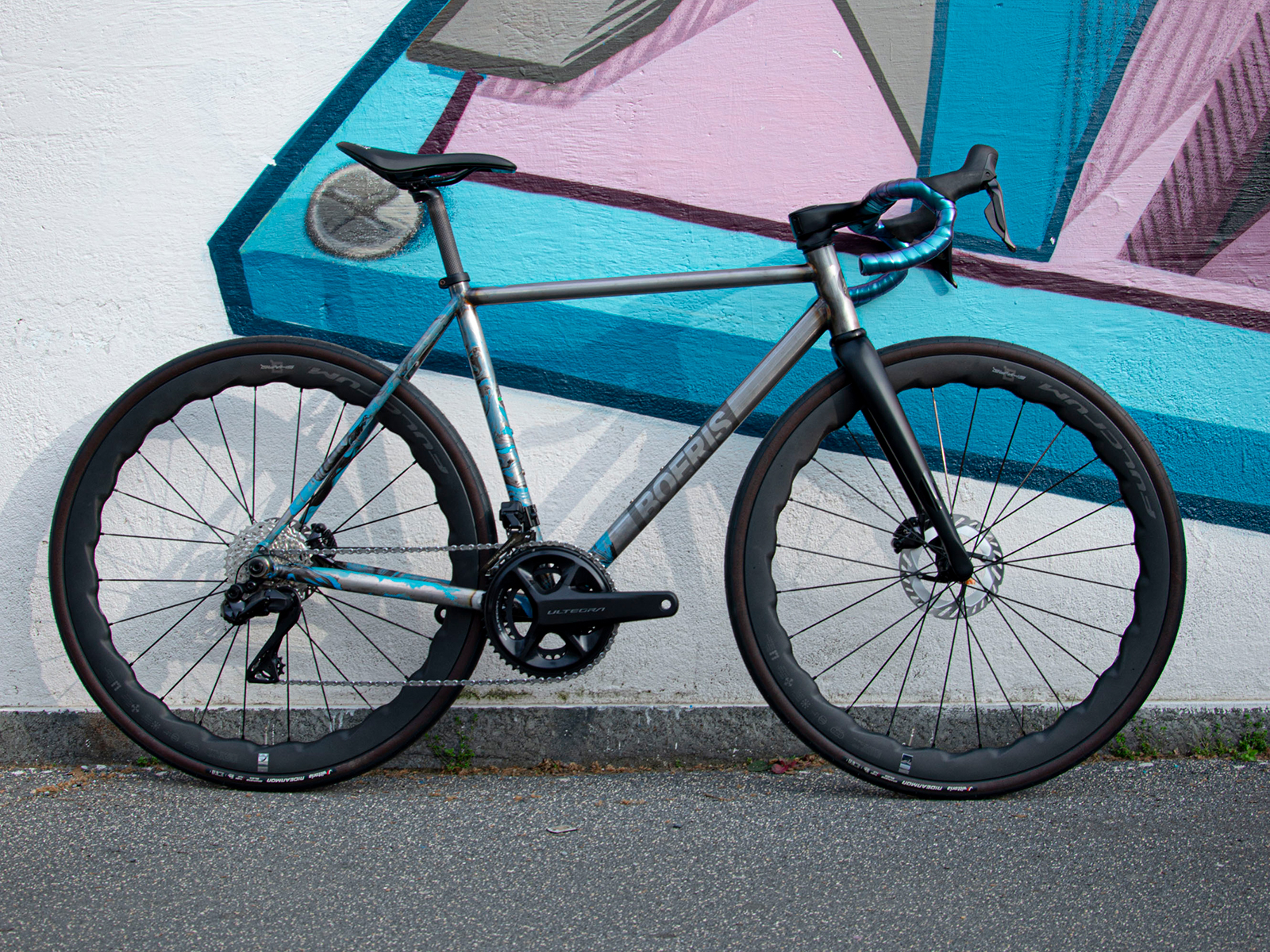 Gravel Serie X grigia in acciaio grigia di Boeris Bikes Torino fotografata al parco Dora appoggiata a un murales azzurro