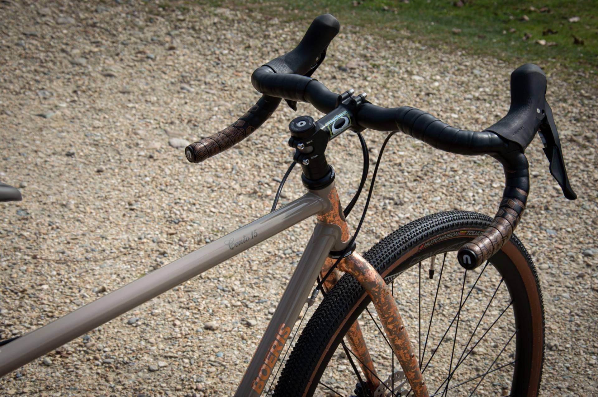 Dettaglio di una gravel serie x beige Boeris Bikes Torino con sella e manubrio marroni vicino ad una siepe