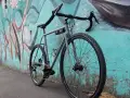 Gravel Serie X grigia in acciaio grigia di Boeris Bikes Torino fotografata al parco Dora appoggiata a un murales azzurro