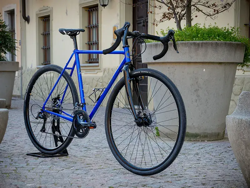 Gravel bike color blu con sella e manubrio neri di Boeris Bikes Torino su un cubettato vicino a fioriere