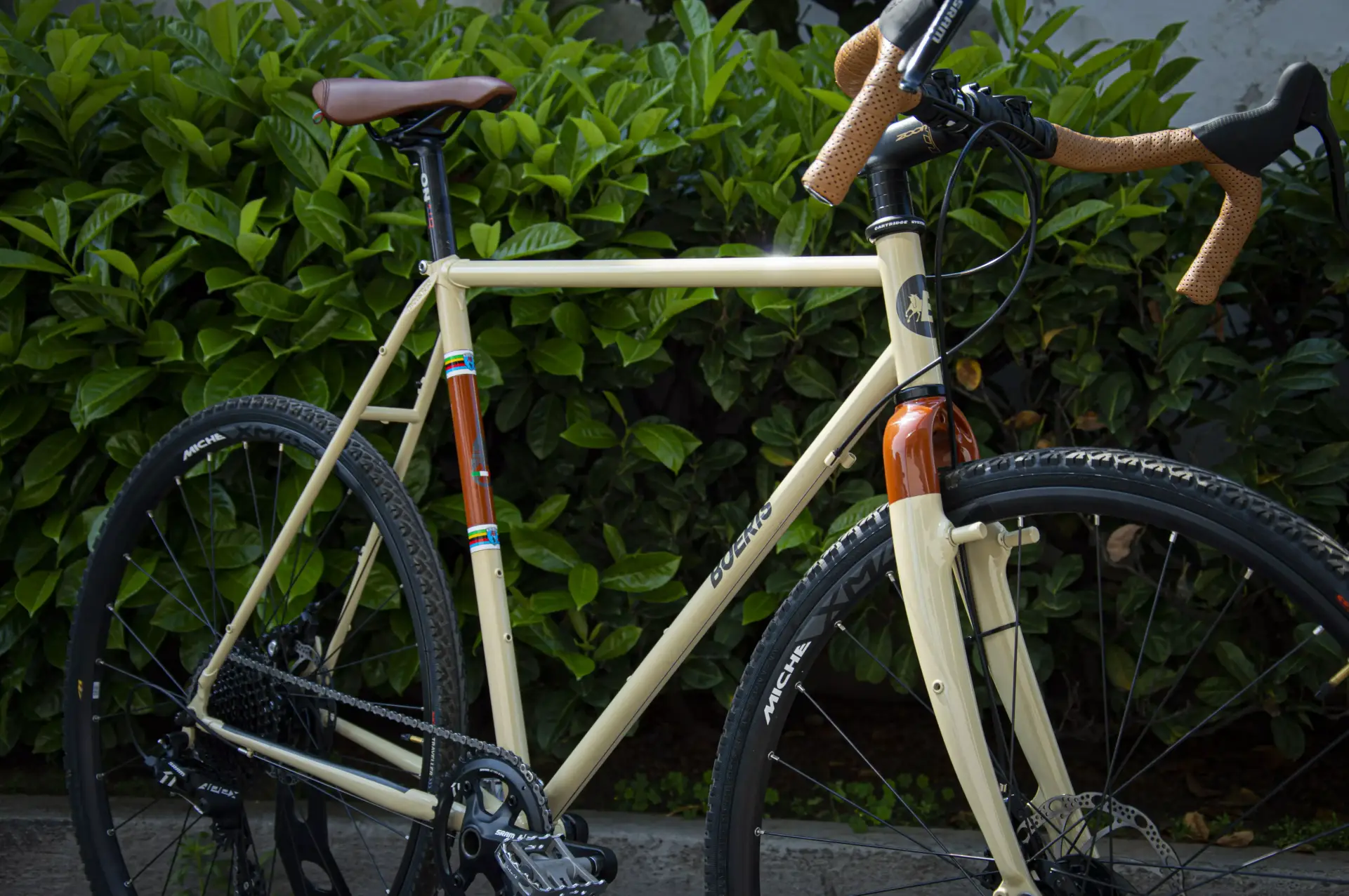 Dettaglio di una gravel serie x beige Boeris Bikes Torino con sella e manubrio marroni vicino ad una siepe