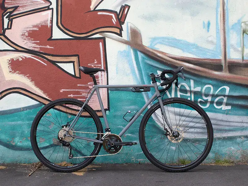 Gravel Serie X grigia in acciaio grigia di Boeris Bikes Torino fotografata al parco Dora appoggiata a un murales azzurro