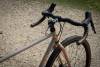 Dettaglio di una gravel serie x beige Boeris Bikes Torino con sella e manubrio marroni vicino ad una siepe